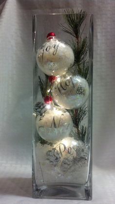 christmas ornaments in a clear glass vase with snow and pine branches on the bottom, which reads joy