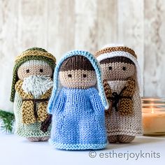 three knitted nativity figurines sitting next to a candle