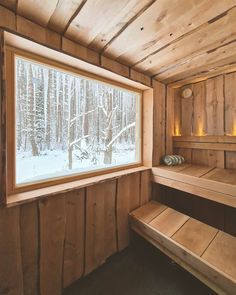 the inside of a wooden cabin with two benches and a window looking out on snow covered trees