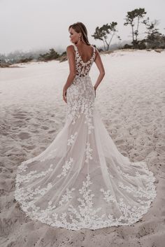 a woman standing on top of a sandy beach wearing a wedding dress with white flowers