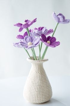 a crocheted vase with purple flowers in it on a white tableclothed surface