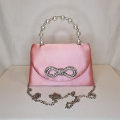 Womens pink top handle evening clutch bag with crystal bow embellishment, crystal and pearl detailed top handle, satin finish material and magnet front closing clasp Can be used with or without long shoulder chain (included) size approx- H 13cm x W 20cm Optional Dust Bag: White lightweight soft polyester portable travel dust bag pouch, suitable for protecting items from dust, dirt, hairs and scratches when not in use size approx- L 47cm x W 31.5cm Material: 100% polyester Please note, there is a Feminine Evening Bag With Pearl Handle For Formal Events, Feminine Evening Bag With Pearl Handle For Formal Occasions, Feminine Pink Clutch For Evening, Feminine Pink Evening Bag For Events, Evening Bag With Pearl Handle And Top Handle Shape, Pink Evening Bag With Pearl Handle For Party, Pearl Handle Top Handle Evening Bag, Glamorous Pink Bags For Formal Occasions, Evening Embellished Pink Bags