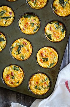 muffin tins filled with eggs and spinach on a wooden table next to a white towel