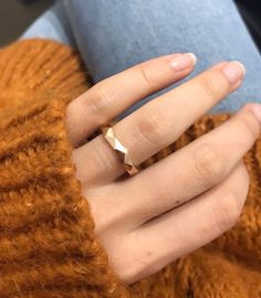 a woman's hand with a gold ring on top of her finger and a brown sweater in the background