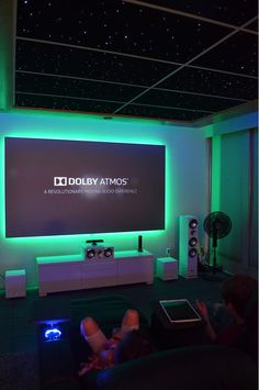 a person sitting in front of a large screen on top of a tv set with the words douby atmos written on it