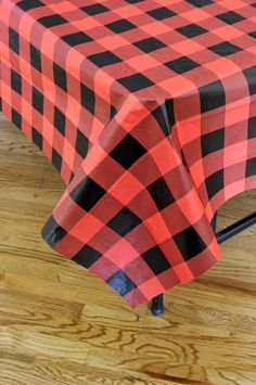 a red and black checkered tablecloth sitting on top of a wooden floor next to a chair