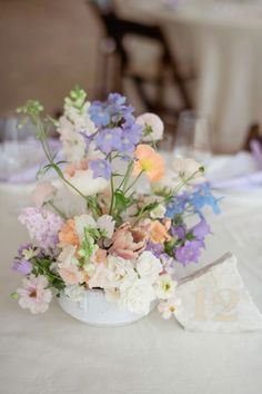 an arrangement of flowers in a white vase on a table with napkins and wine glasses