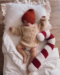 a baby wearing a red and white striped hat is laying on a bed with a stuffed animal