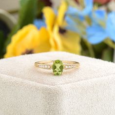 a ring with an oval cut green gems sits on top of a white box next to flowers