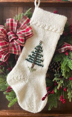 a knitted christmas stocking with a pine tree on it and red plaid bows