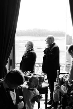 black and white photograph of people standing in front of a window looking out at the water