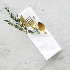 a fork, knife and spoon in a napkin on a marble counter top with greenery