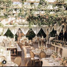 an outdoor dining area with tables and chairs covered in flowers, greenery and white draping