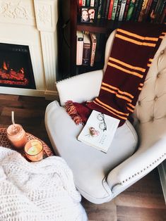 a white chair with a book on it next to a fire place and some candles