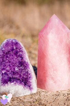 two pink and purple crystals sitting on top of a dirt ground next to each other