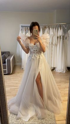 a woman taking a selfie in front of a mirror wearing a wedding dress with high slit