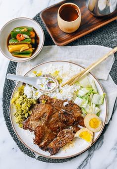 a plate with meat, rice and vegetables on it next to a cup of coffee