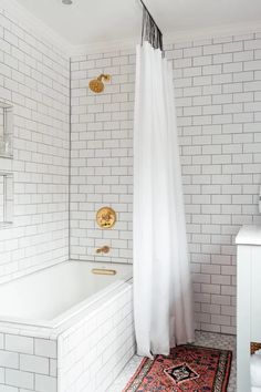 a white tiled bathroom with a rug and bathtub in the corner, along with gold fixtures