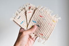 a hand is holding three pieces of woven material with fringes on them, and one piece