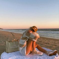 a woman sitting on top of a blanket next to the ocean with a purse in front of her