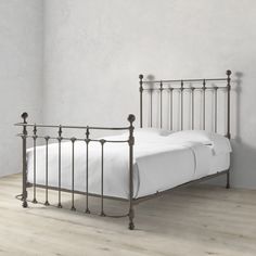 a metal bed frame with white sheets and pillows on top of it in a room