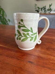 a white coffee cup with green leaves on it sitting on top of a wooden table