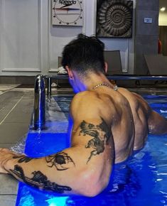 a man with tattoos sitting in a swimming pool