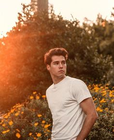 a man standing in front of flowers with the sun behind him and his hands on his hips