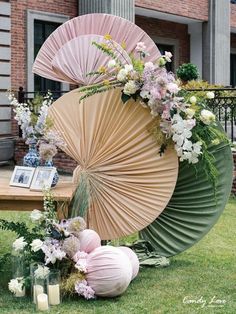 an arrangement of flowers and umbrellas on the grass in front of a brick building