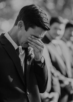 a man in a suit holds his hands to his face as he looks down at the ground