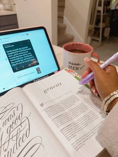 a person is writing on a book with a laptop in front of them and a coffee mug next to it