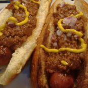 two chili dogs on buns with mustard and onions are sitting on a white plate