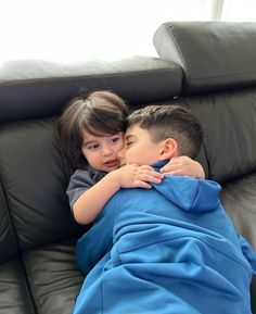 two children are laying on a couch and hugging each other