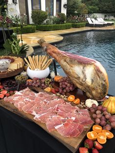 an assortment of meats and fruits on a table next to a pool