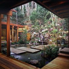 a japanese style garden with a pond and wooden decking, surrounded by greenery