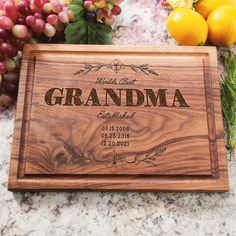 a wooden cutting board with the words grandma engraved on it next to grapes and lemons