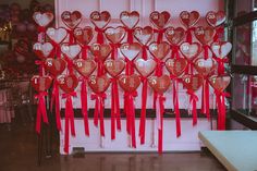 many heart shaped balloons are tied together with red ribbons and bowes on the wall