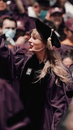 a woman wearing a graduation gown and holding her hand up in the air while standing next to other people