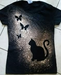 a black t - shirt with a cat and butterflies on it, sitting on the floor