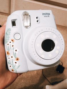 a person holding up a camera with flowers painted on the front and side of it