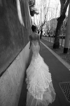 a woman in a wedding dress is walking down the street with her back to the camera