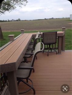 a wooden deck with chairs and tables on it in front of a large grassy field