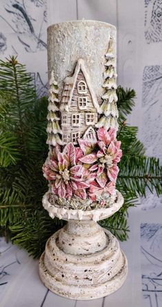 a white candle with pink flowers on it sitting in front of a pine tree and snow covered wall