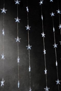 some white and blue stars are hanging from a string on a black wall with lights