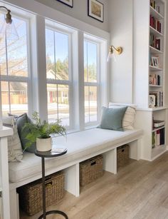 a white window seat with two plants on it and some bookshelves in the background