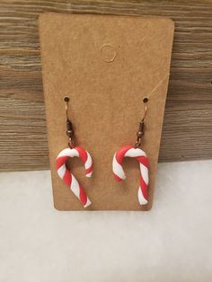 red and white candy cane earrings on a brown card with a wooden box in the background