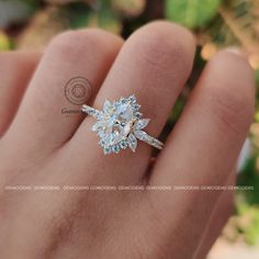 a woman's hand holding an engagement ring with a flower design on the side