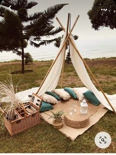 a teepee sitting on top of a lush green field next to the ocean with pillows and blankets