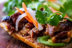 a sandwich with meat, carrots and cilantro is on a cutting board