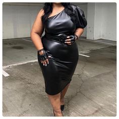 a woman in a black leather dress posing for the camera with her hands on her hips